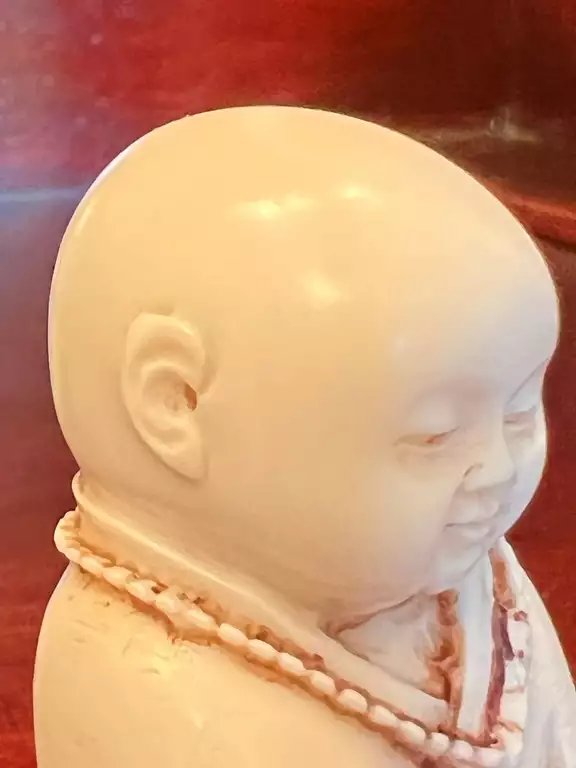 Weiße Figur eines lächelnden Mönchs mit geschlossenen Augen, das Ohr im Mittelpunkt