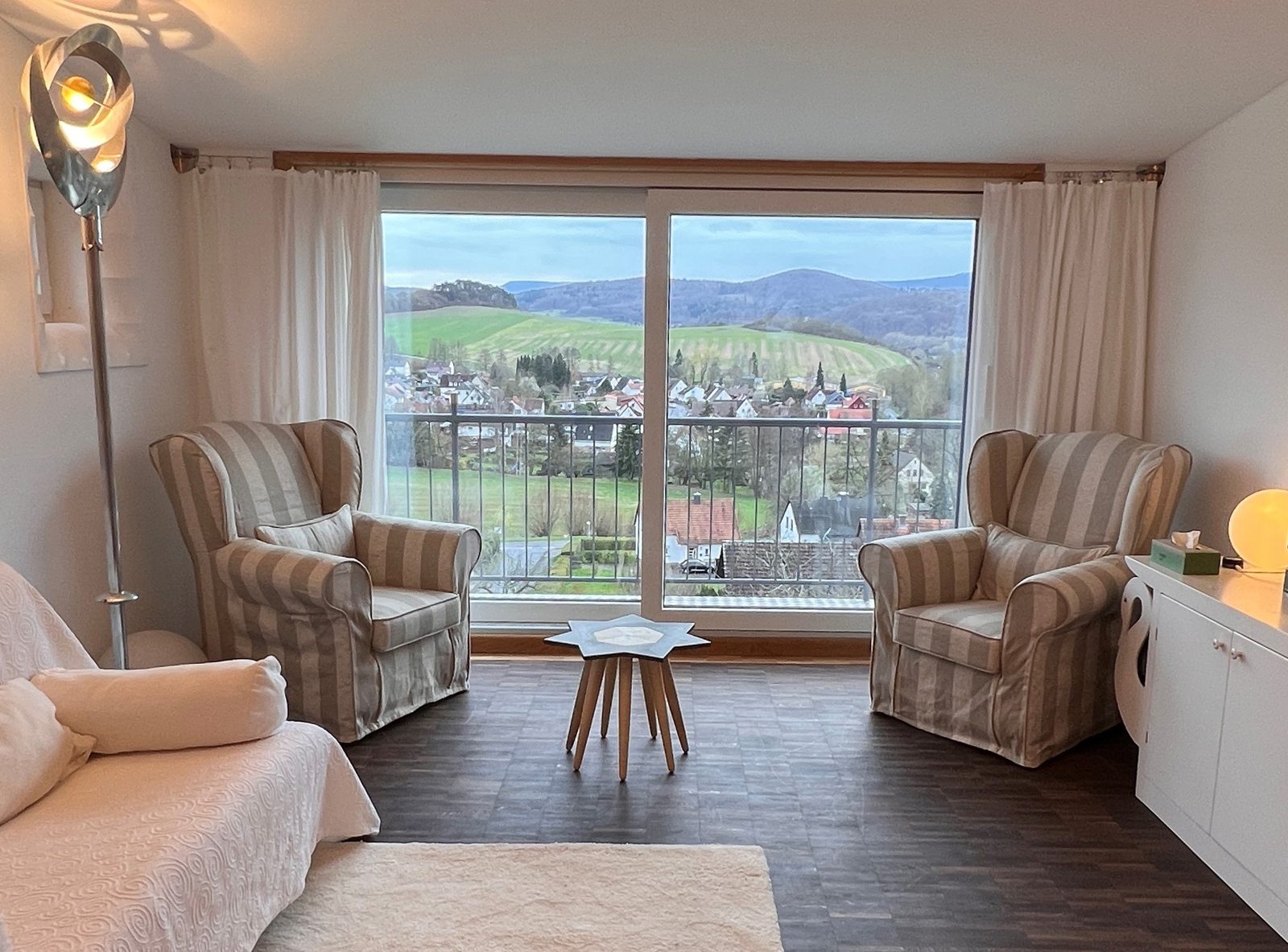 Praxisraum mit zwei Sesseln vor einem großen Fenster mit Blick über den Ort auf die Hügel