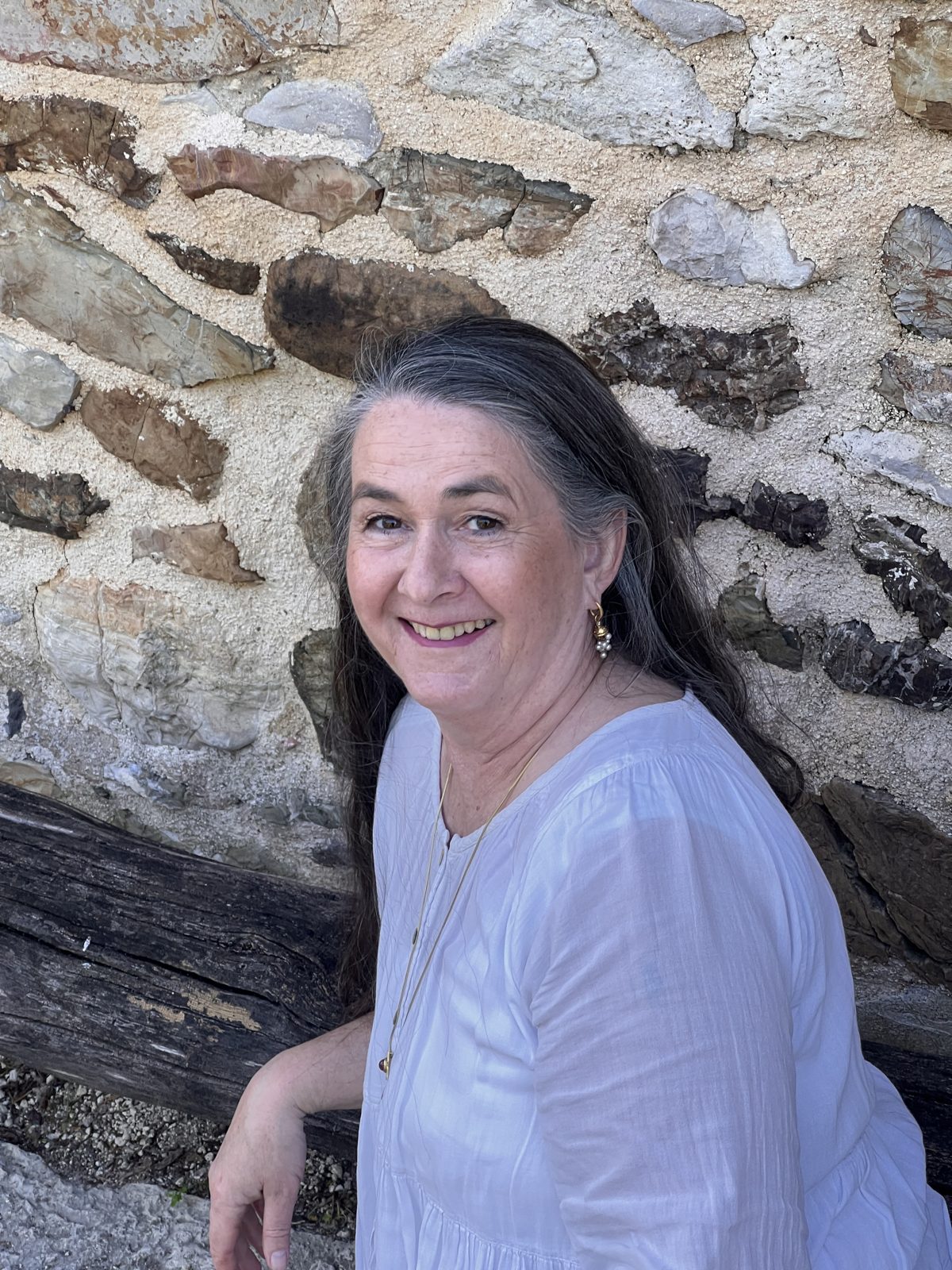 Coco Caroline Heinrichs lächelnd vor einer alten Natursteinmauer